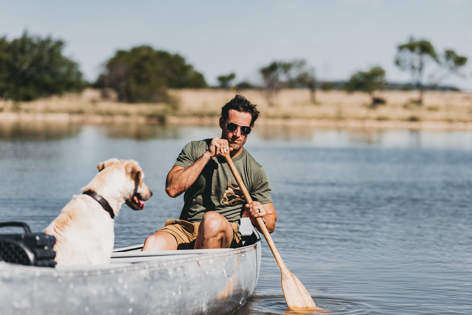 Man paddling a canoe with a dog on a calm lake