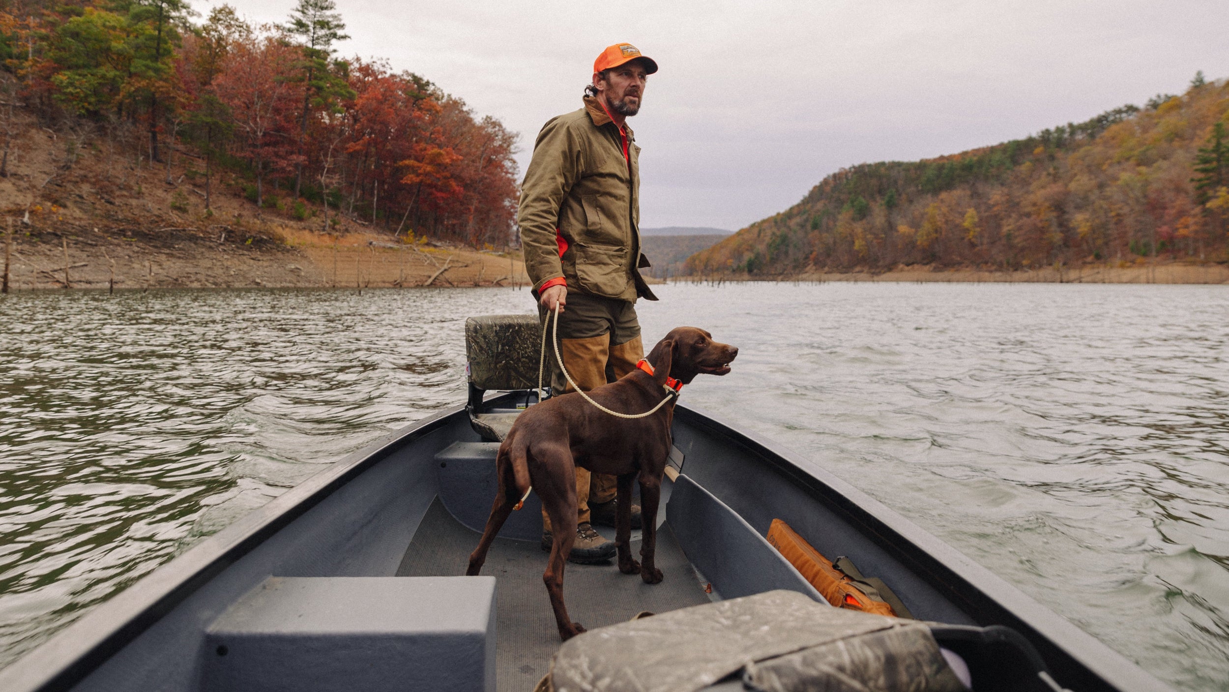 Man with a dog on a boat in a lake surrounded by trees