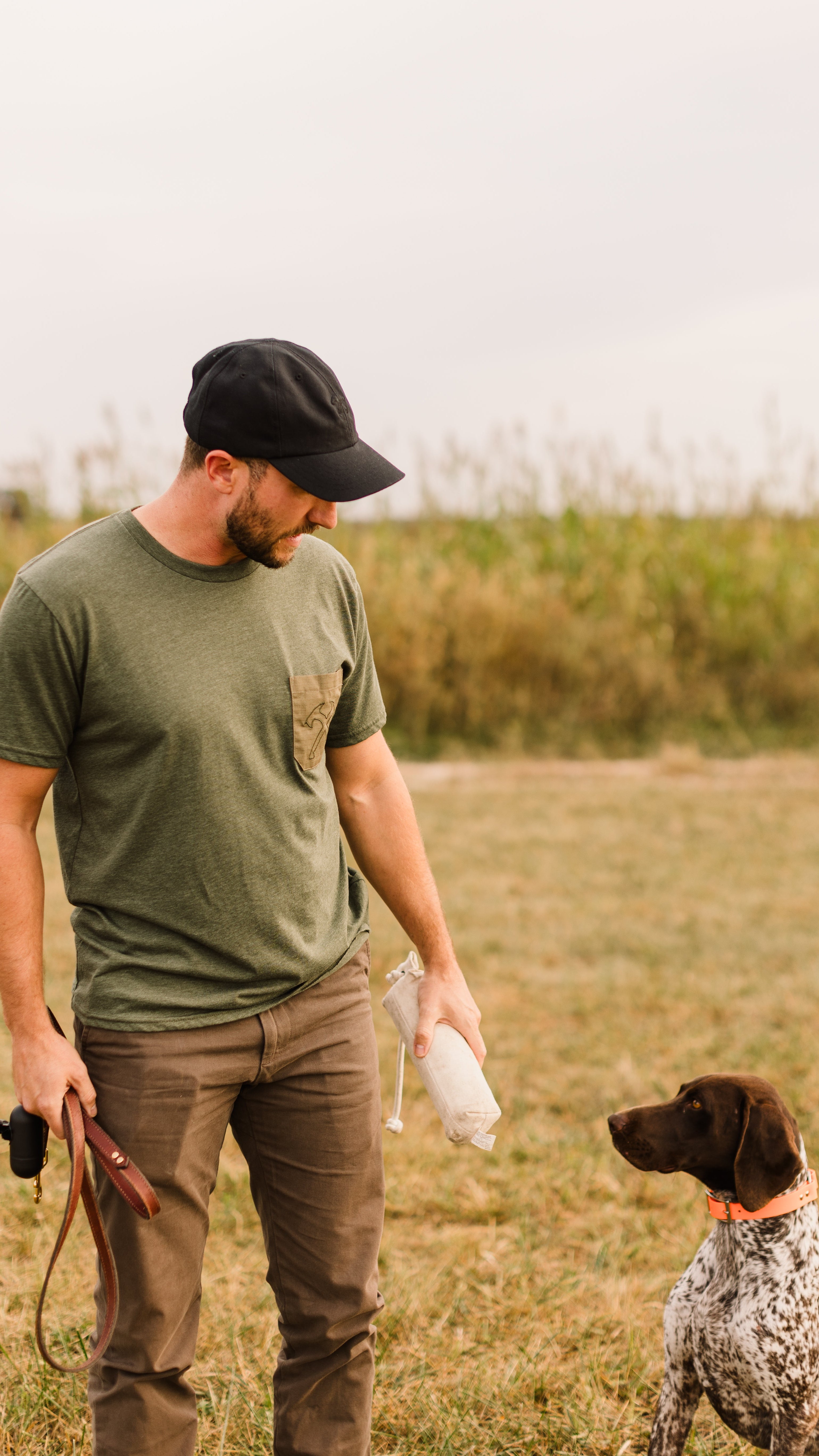 Man in a green shirt and cap standing with a dog in a field