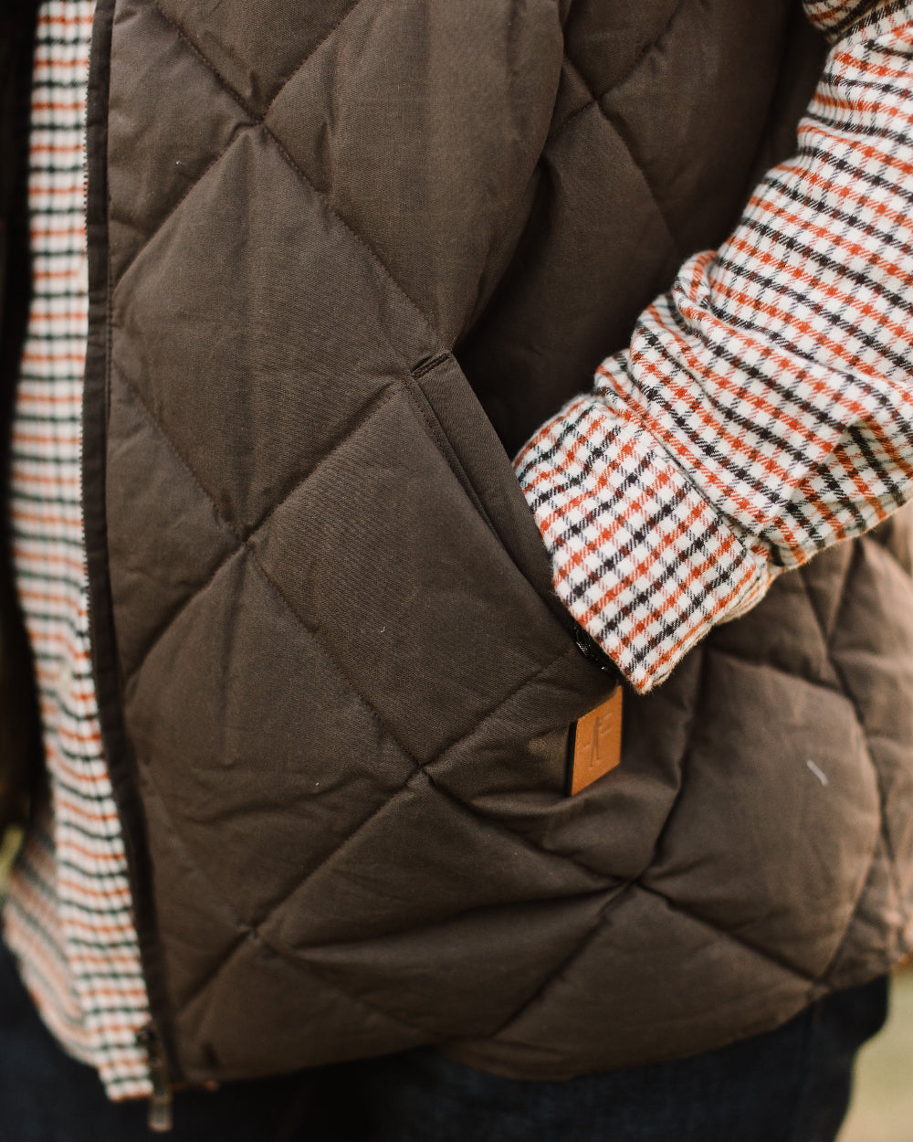 Brown quilted jacket with plaid lining and brand tag, close-up view.