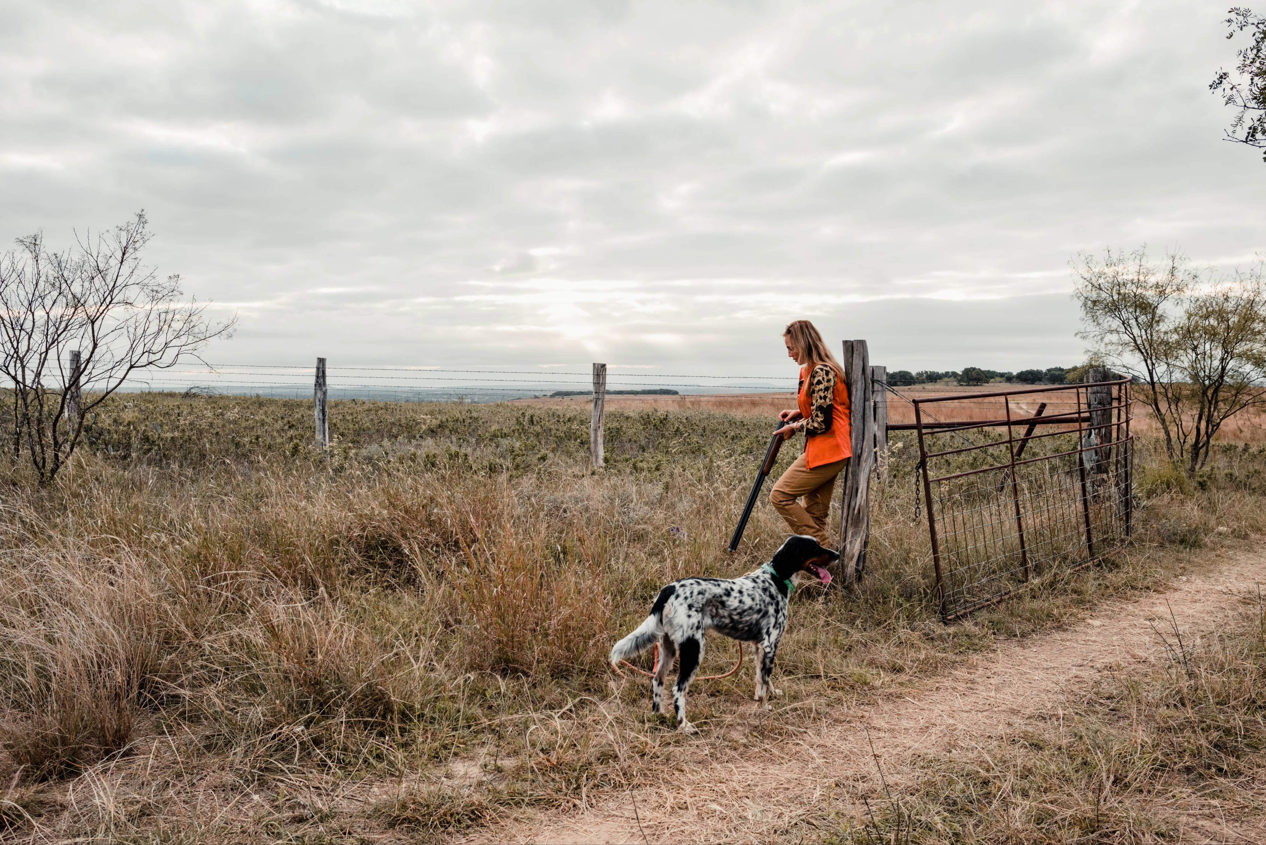 Person in orange vest with a dog walking on a dirt path in a field