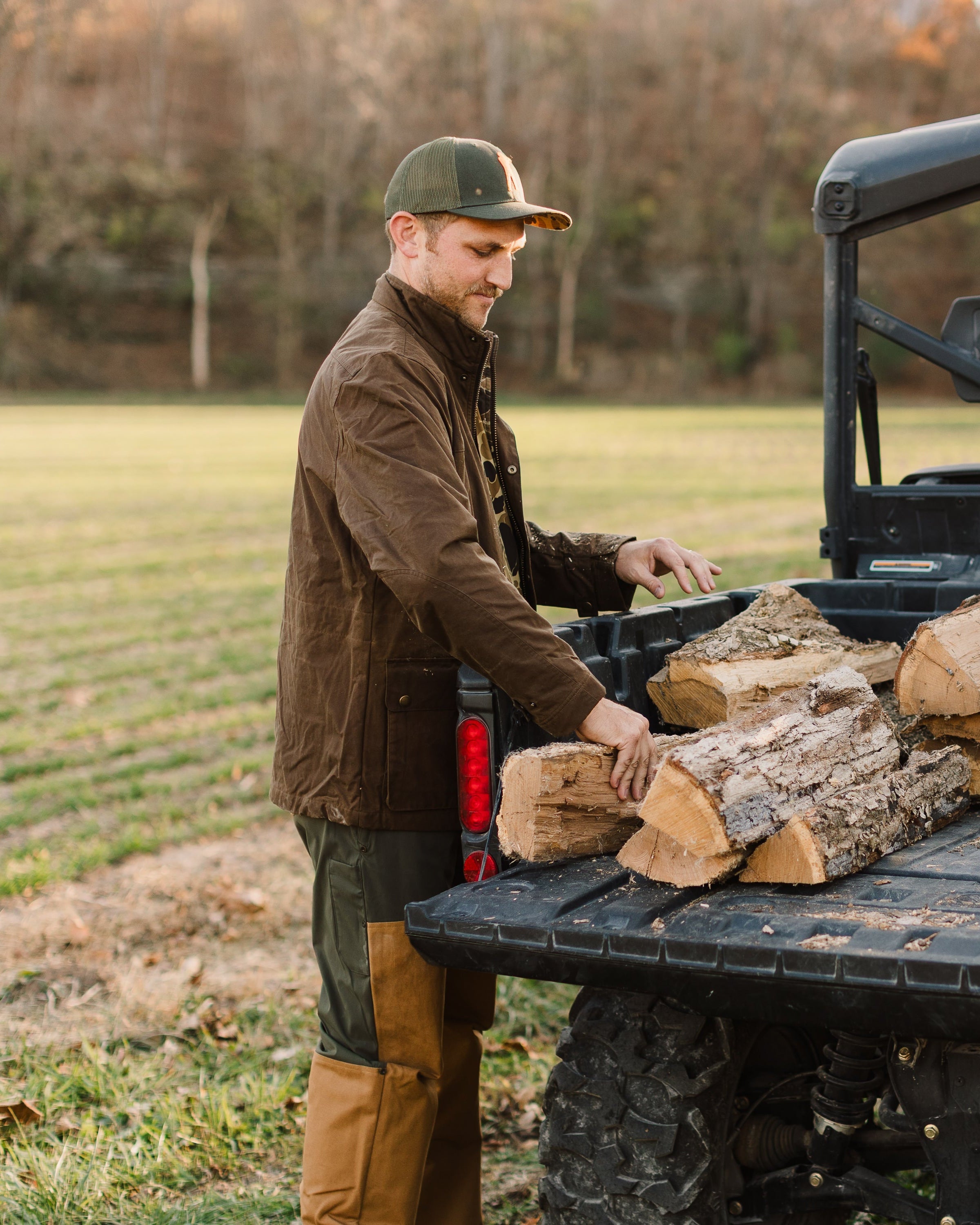 Man loading firewood into the back of a pickup truck in an open field.